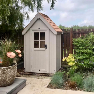 Small garden shed with a shingled roof in a backyard setting.